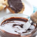 Titled image of sugar-free Nutella in a glass jar with a muffin on a plate in the background.