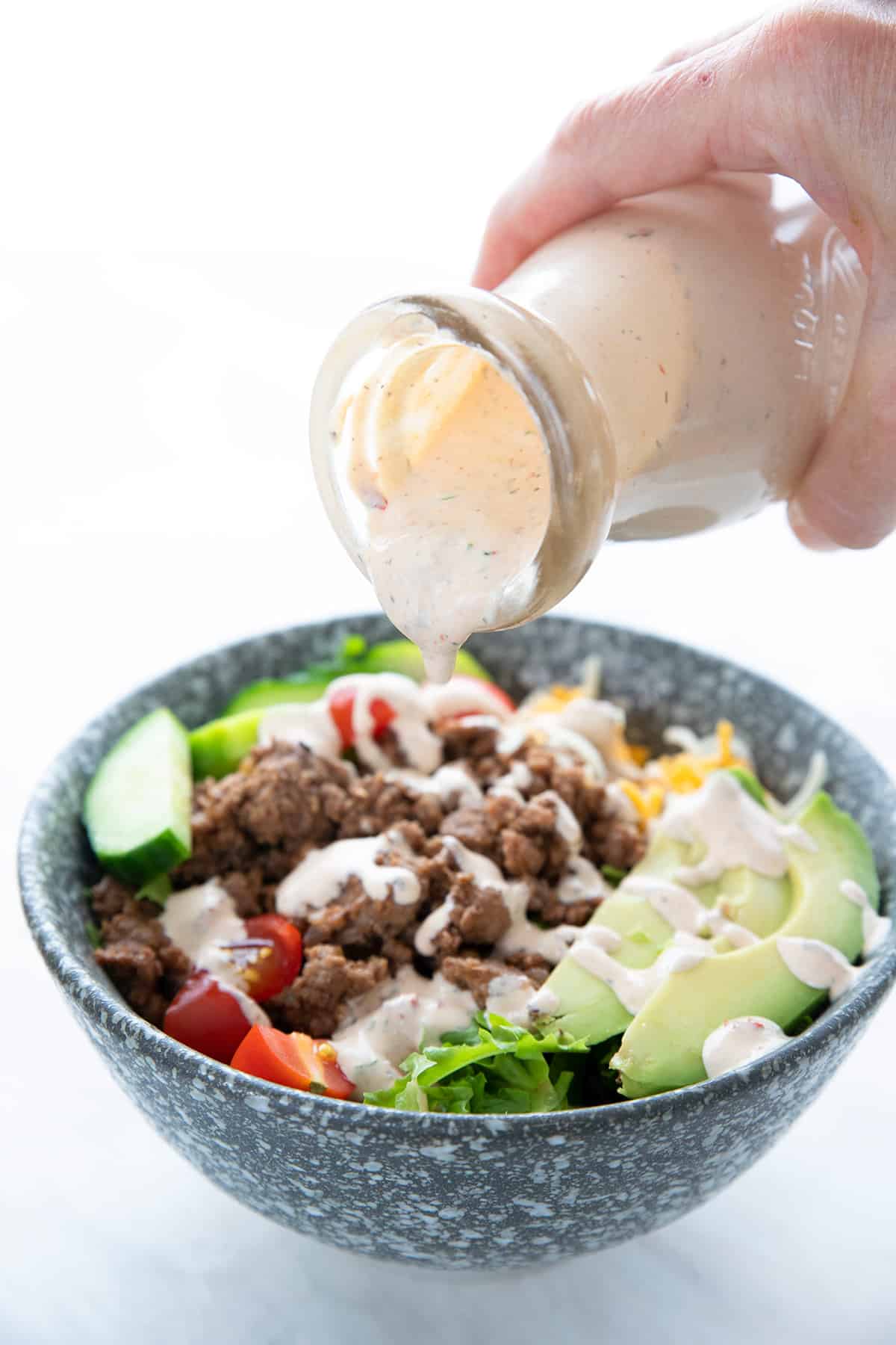Chipotle ranch dressing being drizzled over a bowl of salad.