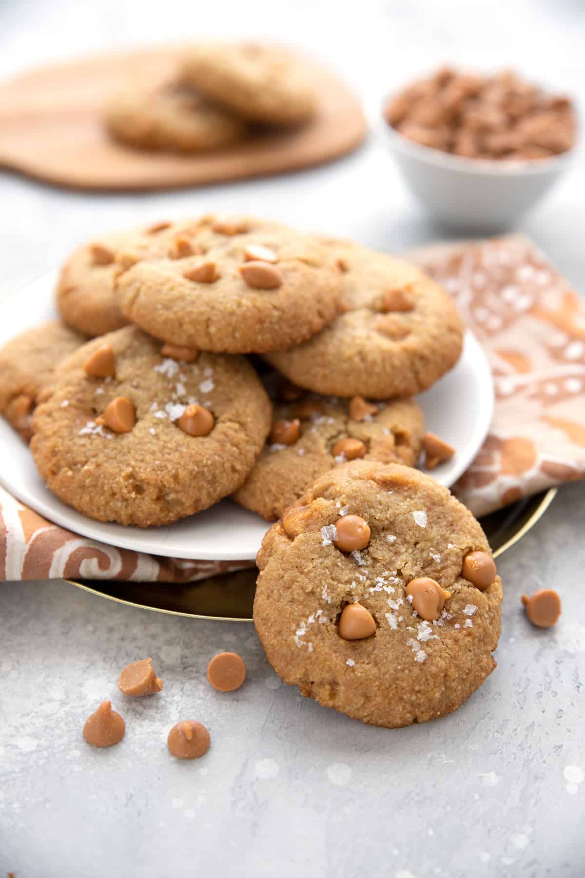 Keto Butterscotch Cookies on a white plate with one cookie in front and some butterscotch chips strewn around.