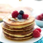 A stack of keto coconut flour pancakes on a white plate, with berries on top.