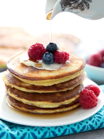 A stack of keto coconut flour pancakes on a white plate, with berries on top.