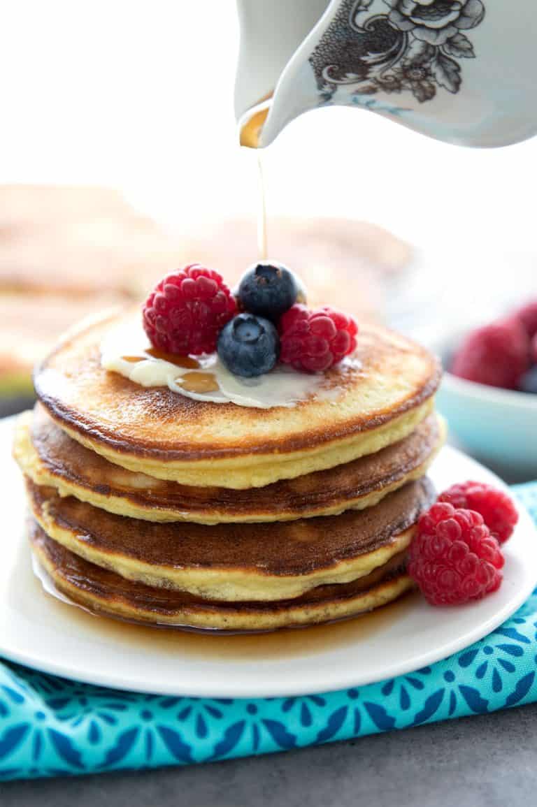 A stack of keto coconut flour pancakes on a white plate, with berries on top.