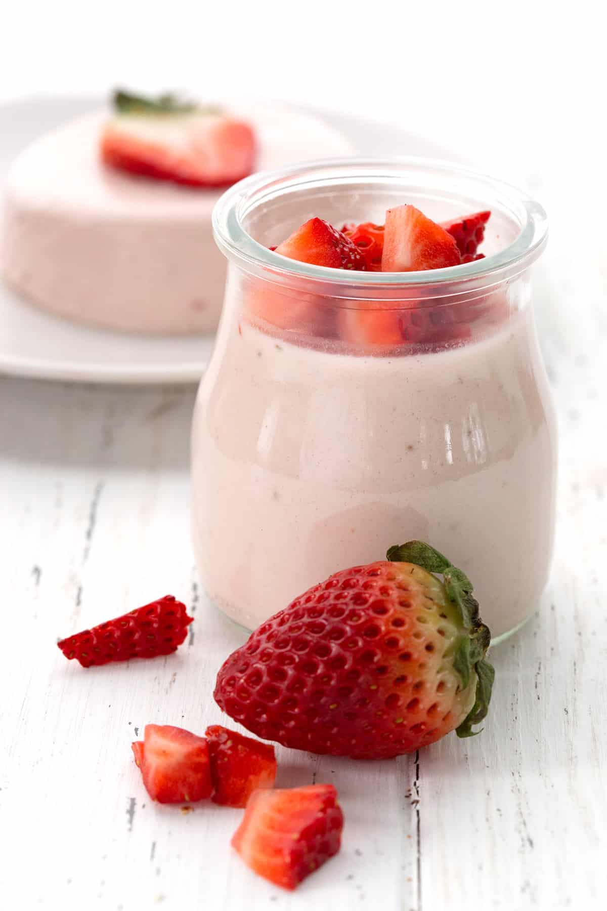 A glass jar filled with keto strawberry panna cotta, with chopped strawberries on top.