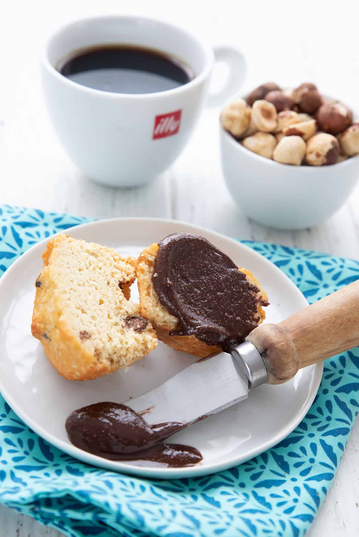 A keto muffin on a white plate, spread with sugar free nutella.