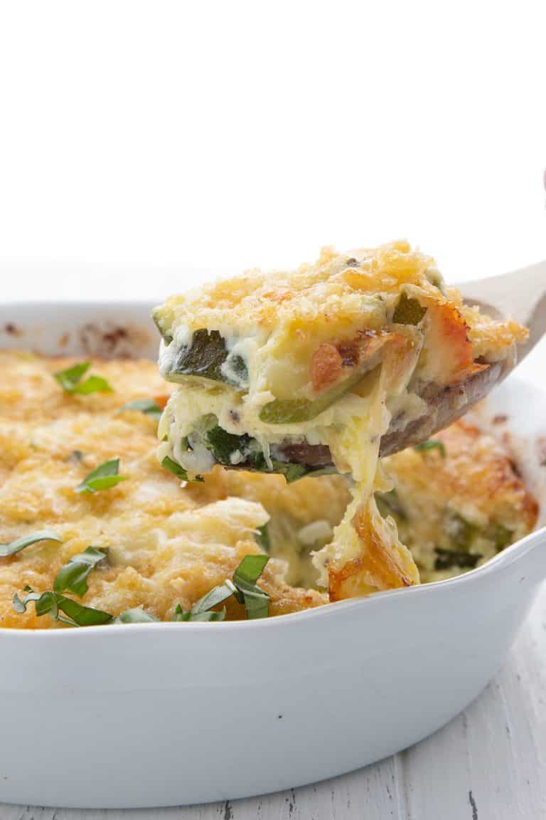 A wooden spoon lifting a serving of zucchini casserole out of a baking dish.