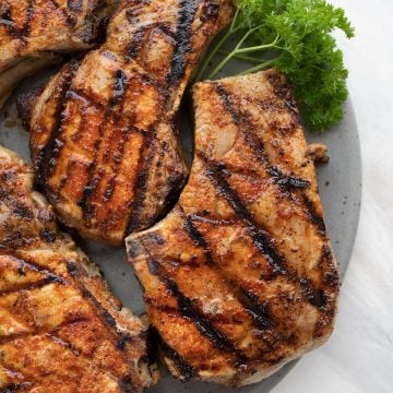 Top down image of grilled pork chops on a gray plate over a marble table.
