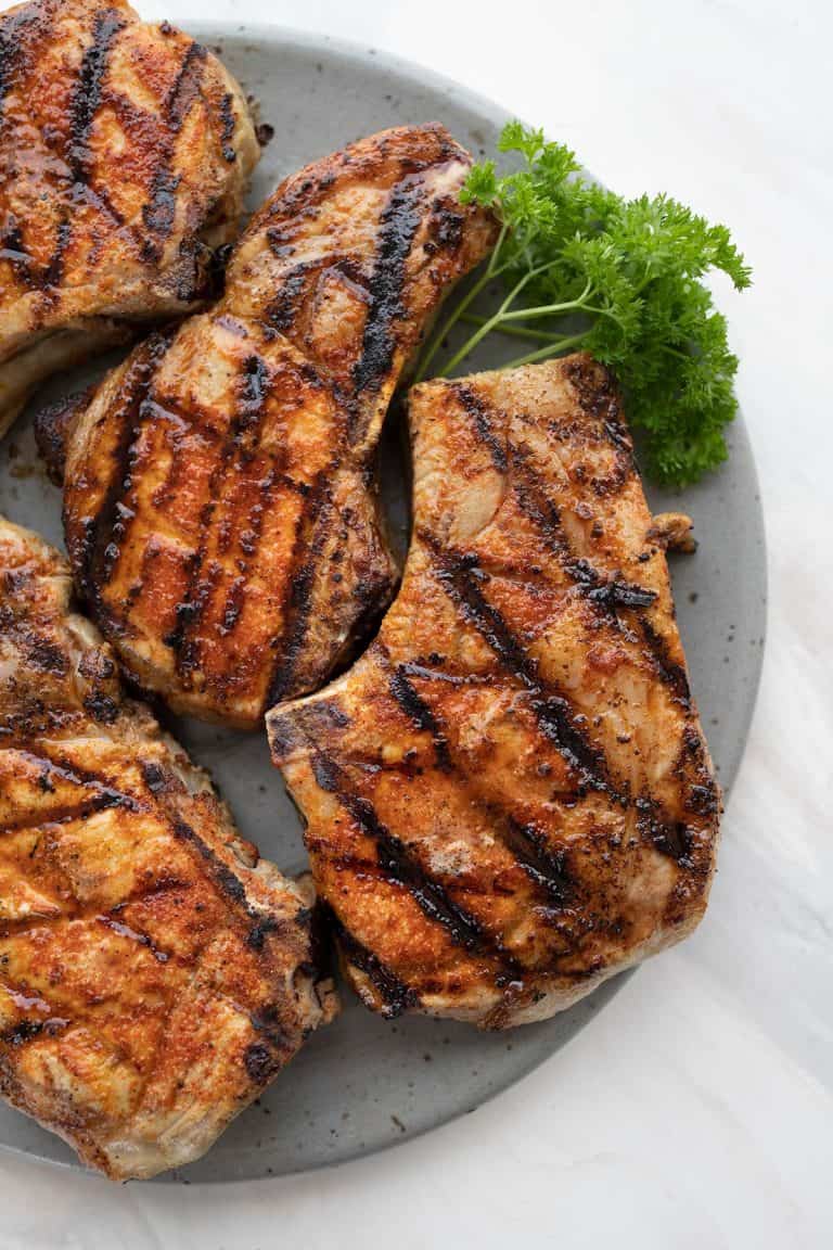 Top down image of grilled pork chops on a gray plate over a marble table.