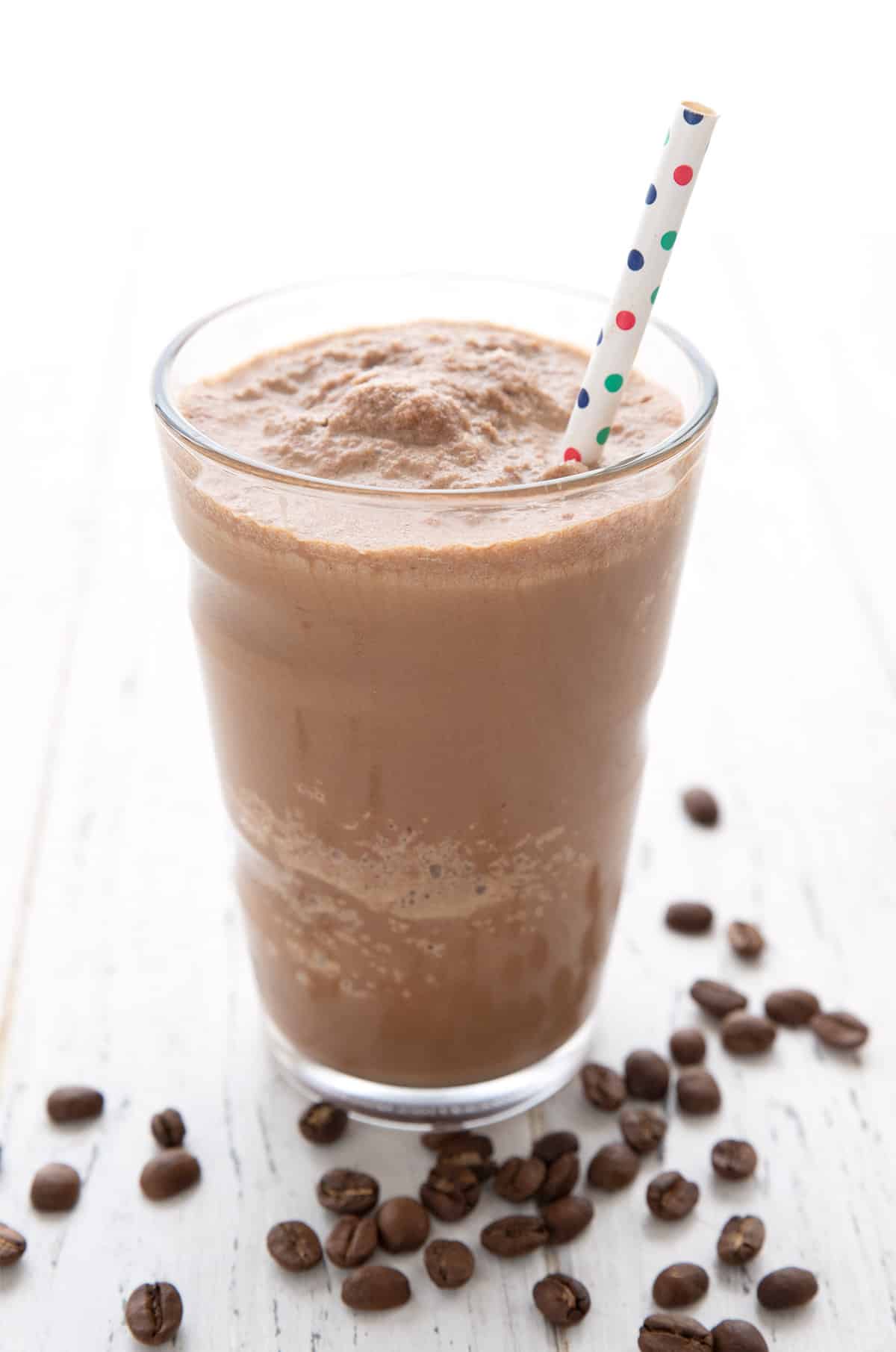 Enkel keto-proteinshake med kaffe i et høyt glass med et strå med polkaprikker. 