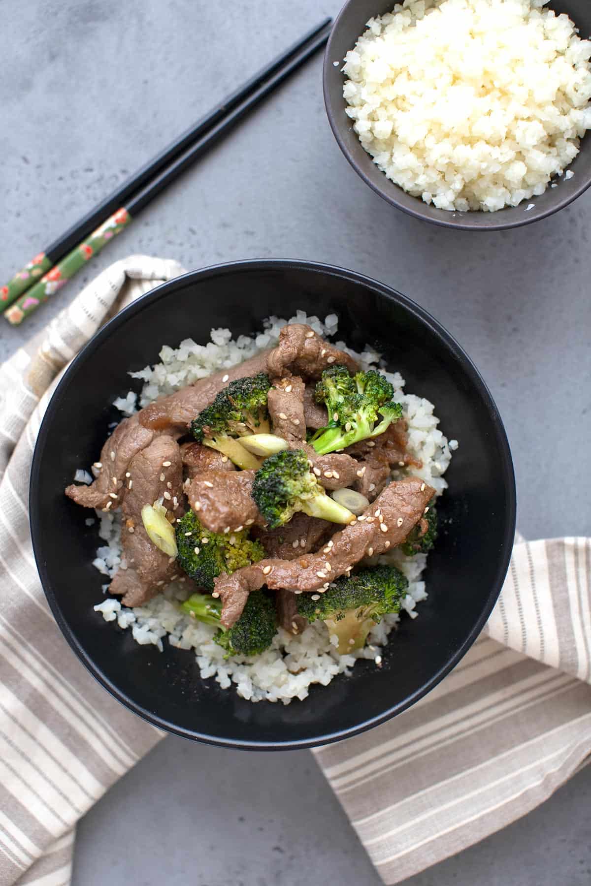 Top down image of a bowl of keto beef and broccoli over cauliflower rice with a pair of chopsticks. 