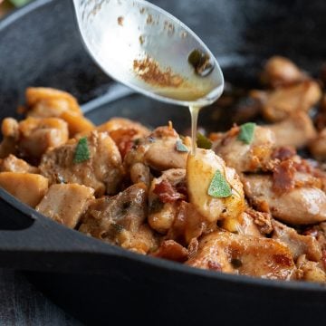 A spoon pouring brown butter over chicken in a cast iron skillet.