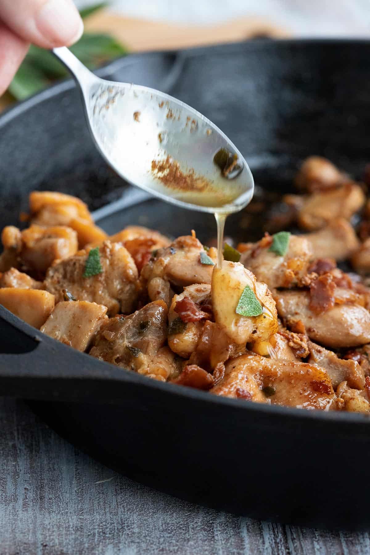 A spoon pouring brown butter over chicken in a cast iron skillet.