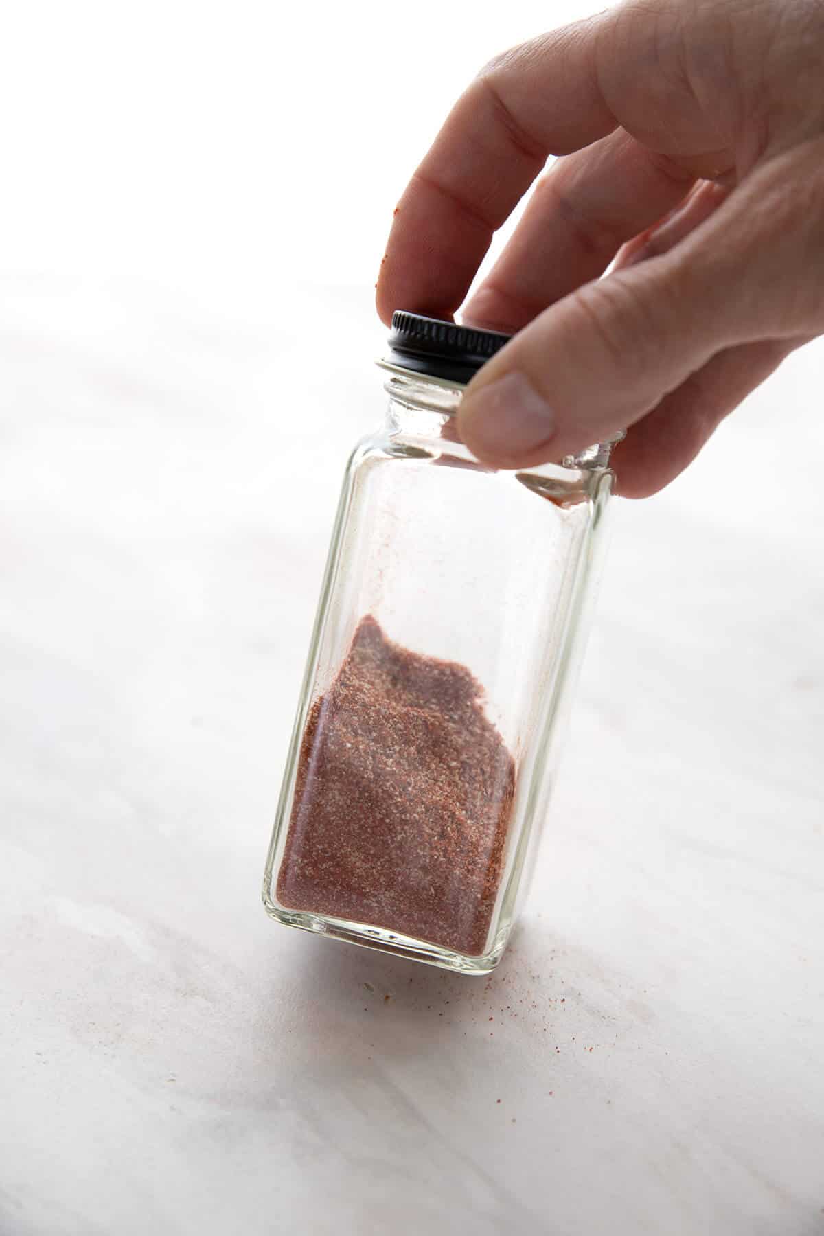 Hand holding a glass spice jar with spice mixture in it