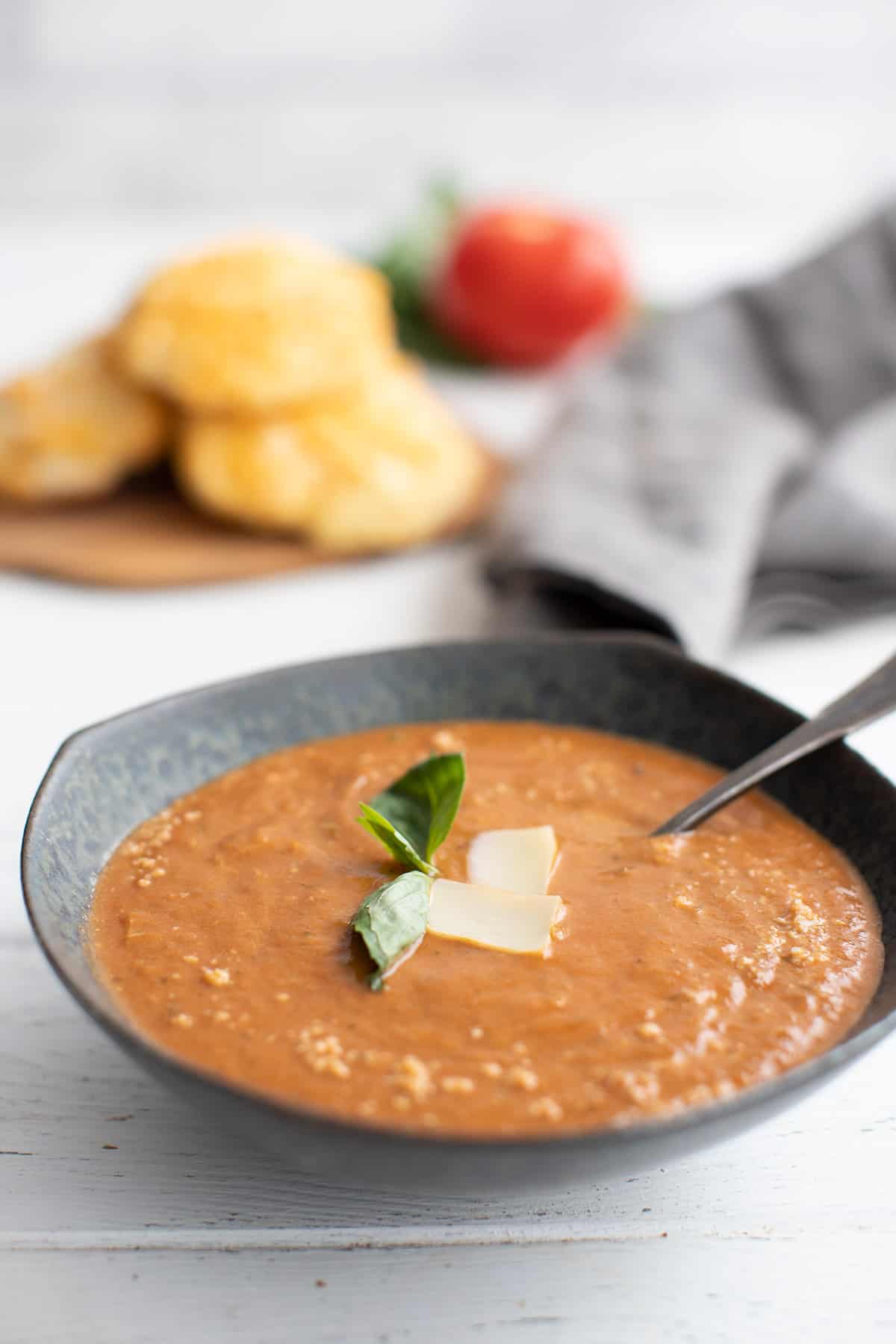 A bowl of keto roasted tomato  soup in front of a cutting board piled with keto biscuits. 