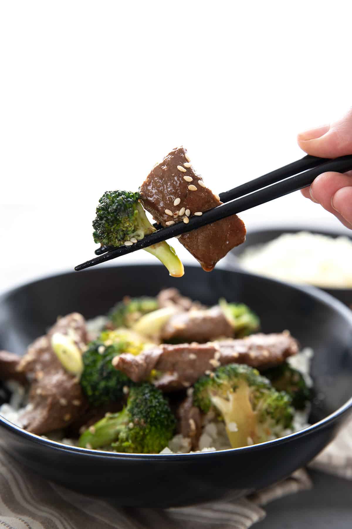 Chopsticks holding up keto beef and broccoli above a bowl. 