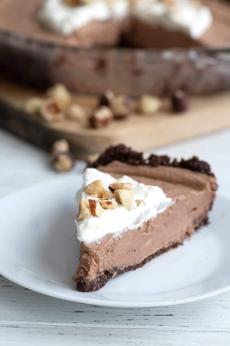 A slice of Keto Nutella Cream Pie on a white plate, with the rest of the pie in the background.