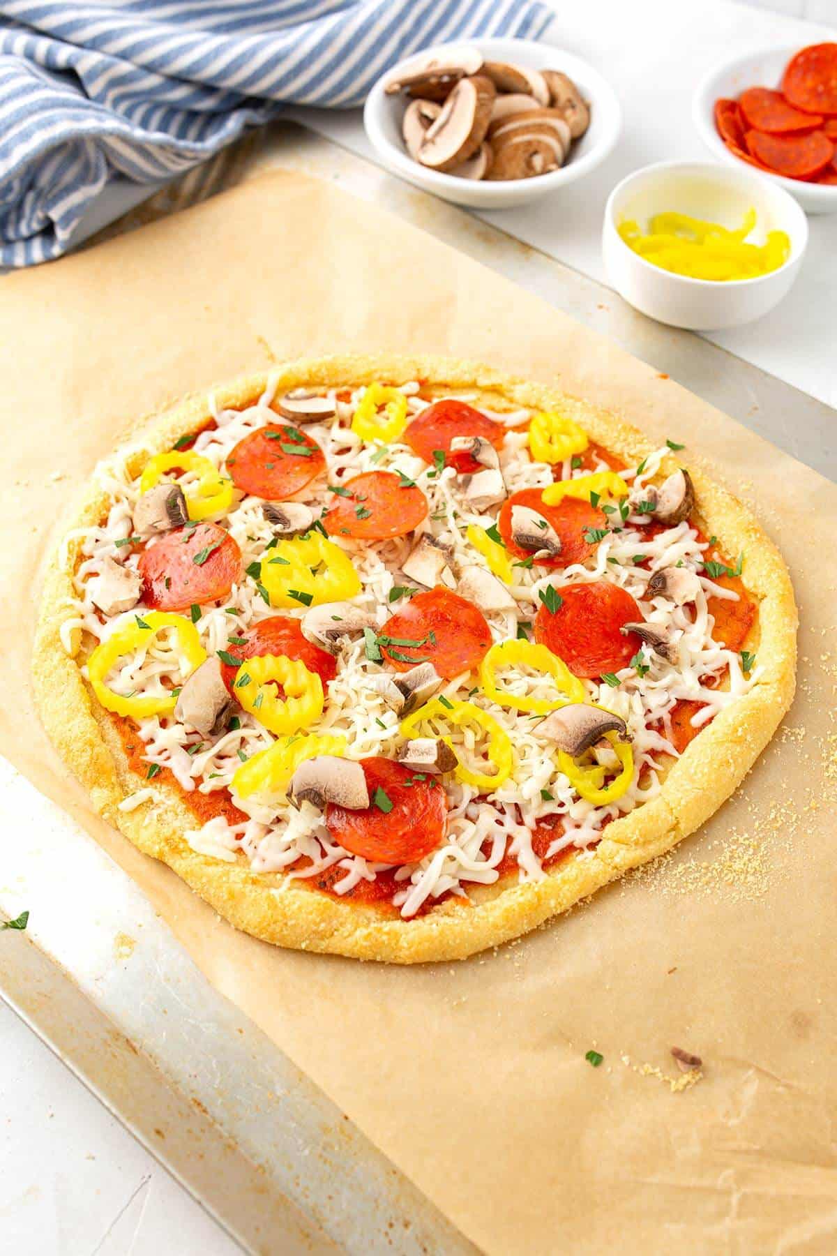 A round keto pizza topped with pepperoni, mushrooms and banana peppers ready to be baked