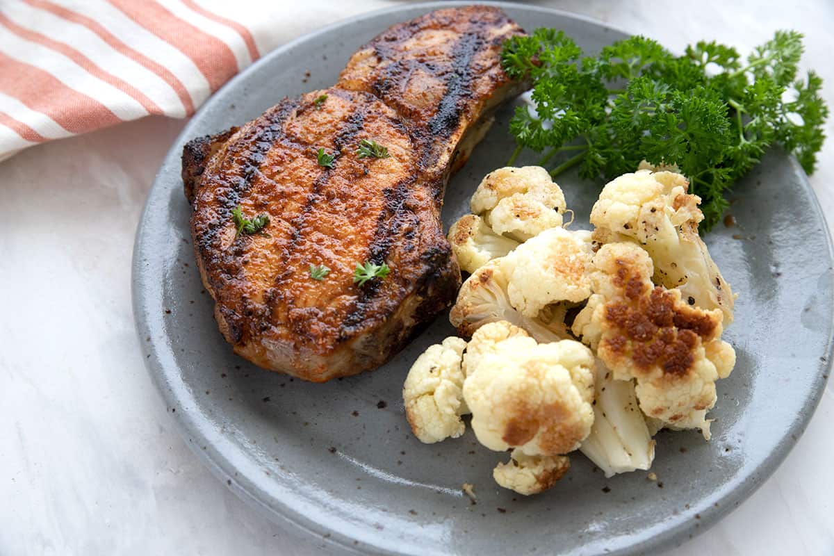 A gray plate holding a grilled pork chop and roasted cauliflower.