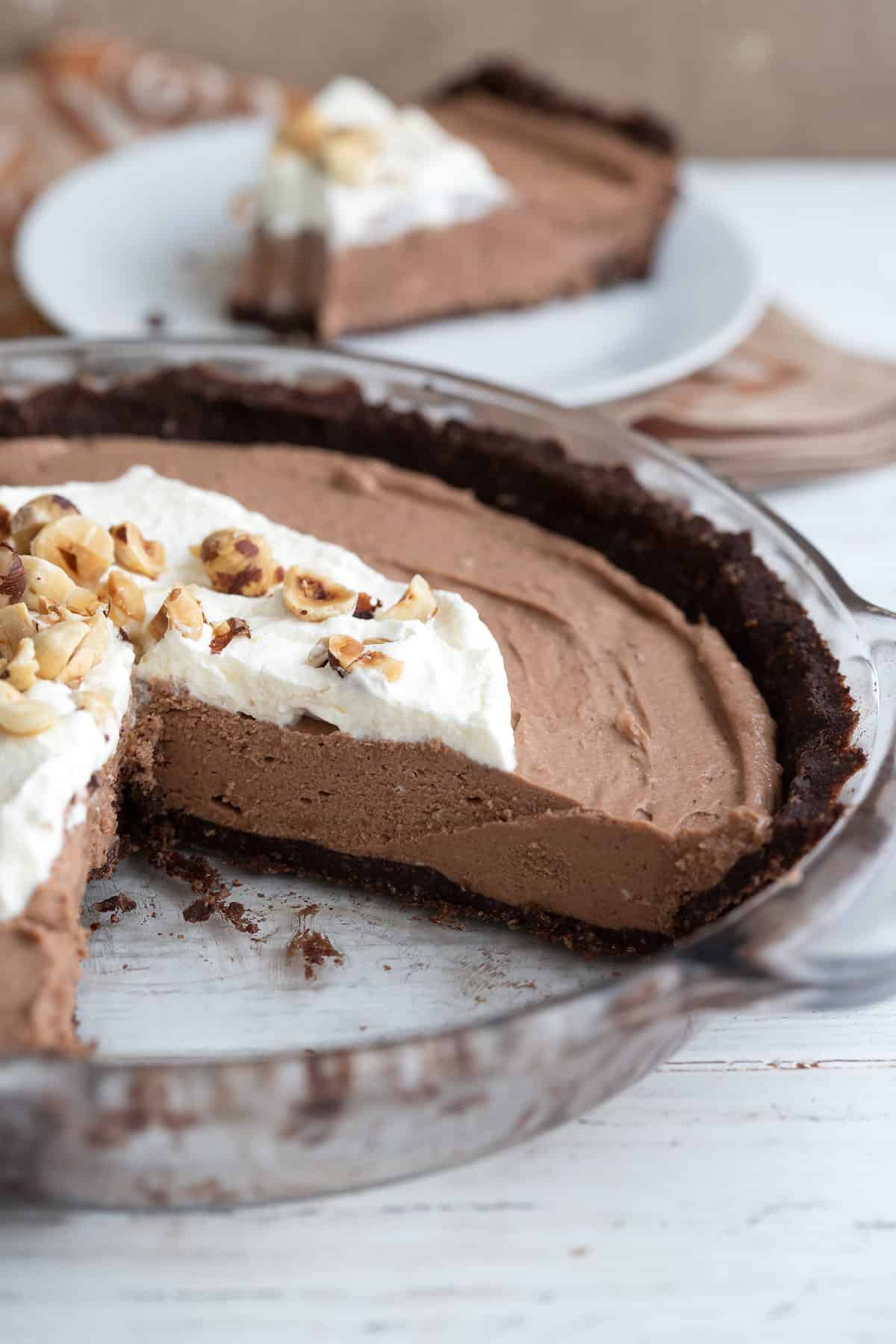 No Bake Hazelnut Cream Pie in a glass pie plate on a white wooden table, with two slices cut out of it. 