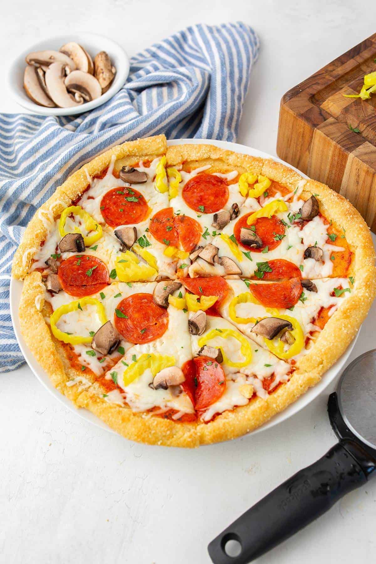 Three quarter shot of a freshly baked whole keto pizza topped with pepperoni, mushrooms and banana peppers