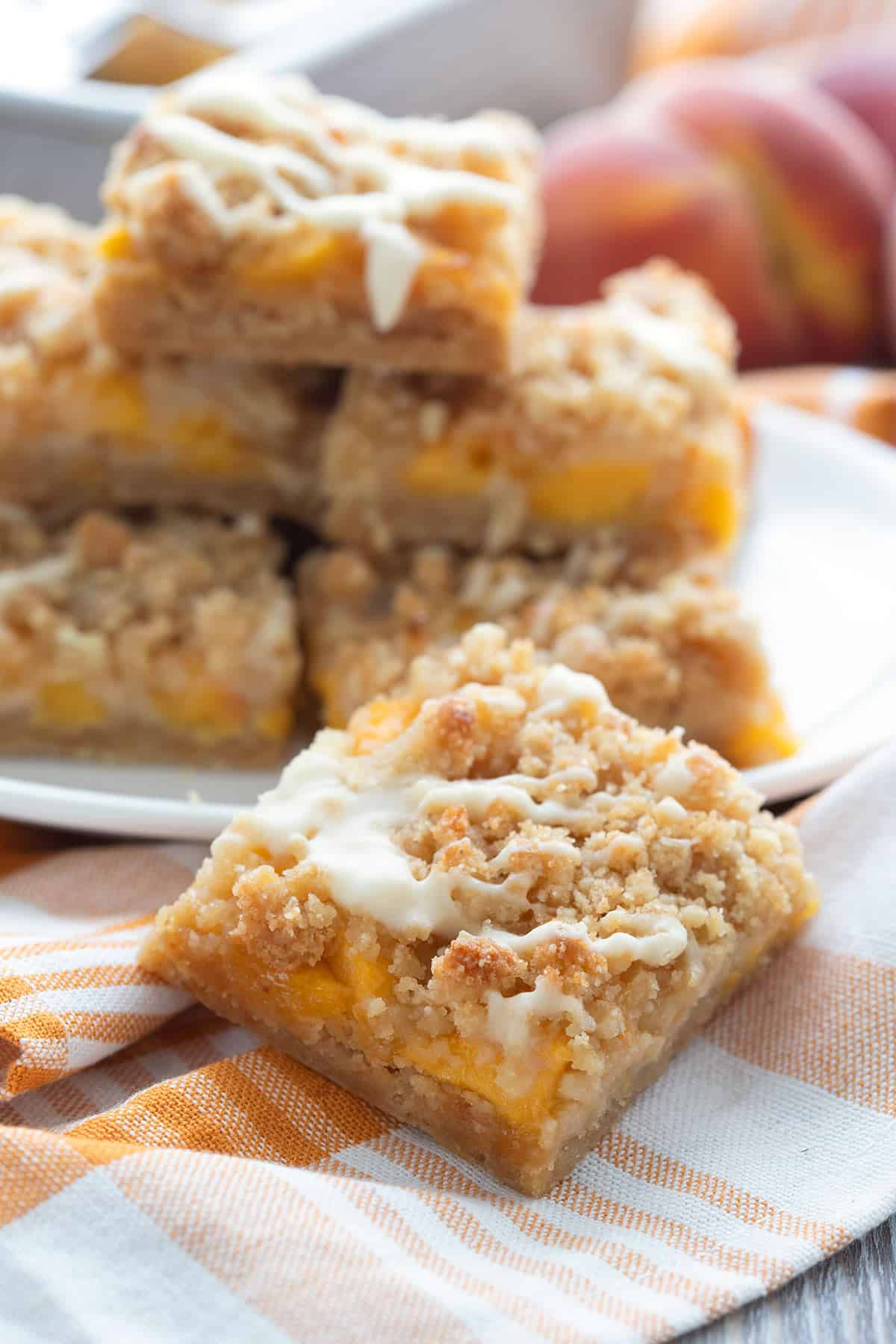 A peach cobbler bar sits in front of a white plate of more bars. 