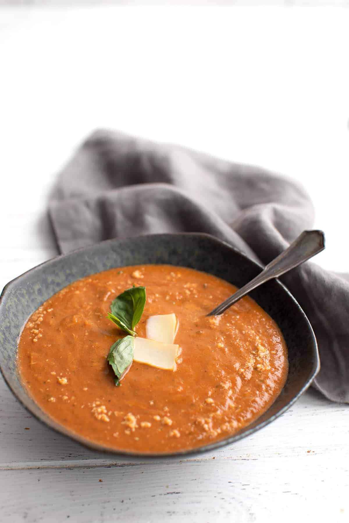 A black bowl filled with creamy Keto Tomato Soup, topped with parmesan and basil. 