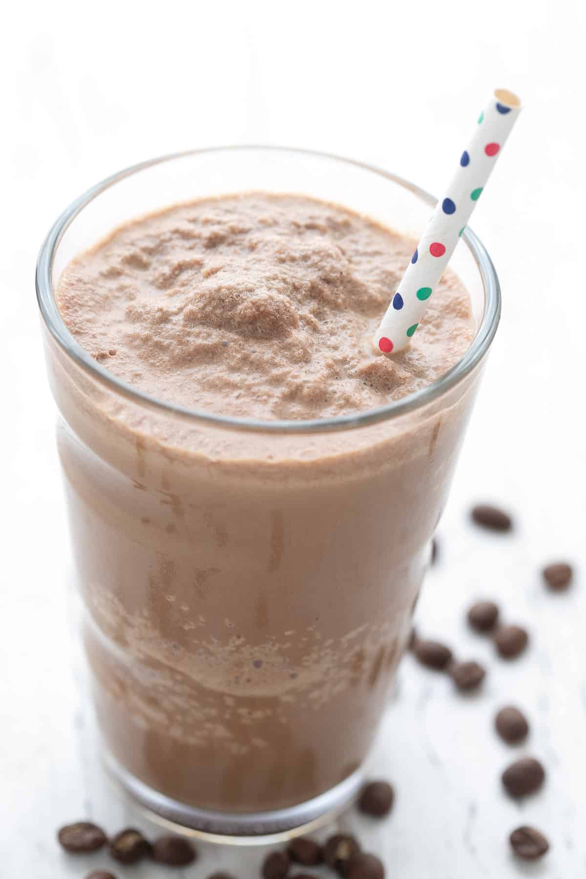 Nærbilde av en keto-kaffeproteinshake i et høyt glass med sugerør. 