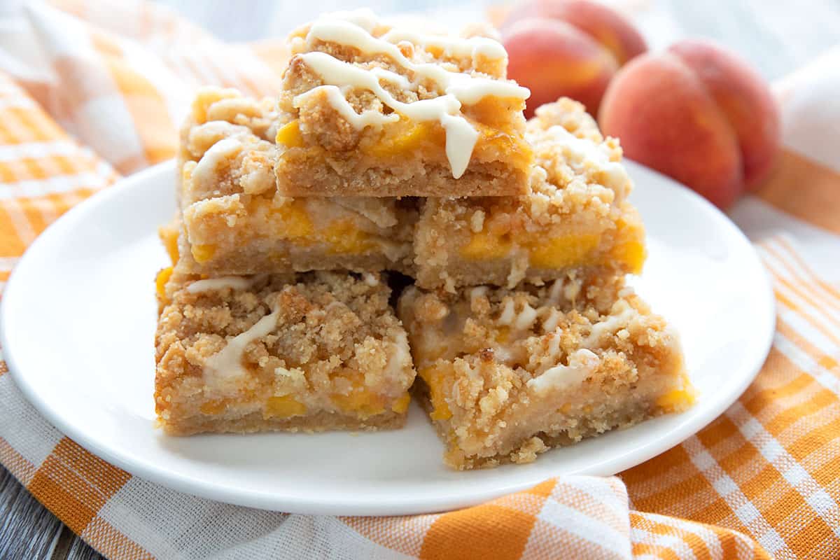 Peach cobbler bars on a white plate with peaches in the background. 
