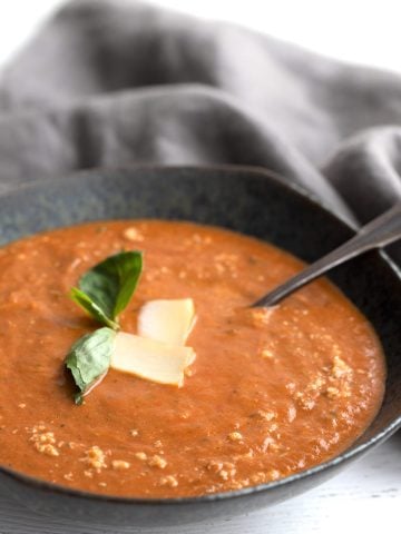 Close up shot of a bowl of Roasted Tomato Soup with basil and Parmesan.