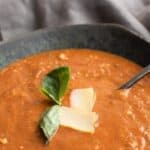 Titled image of a black bowl filled with keto roasted tomato soup, with shaved parmesan and basil leaves on top.