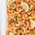 Top down image of Easy Baked Shrimp in a white baking dish with slices of lemon.