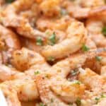 Titled Pinterest Image: Close up shot of Parmesan Baked Shrimp in a white baking dish with chopped parsley.