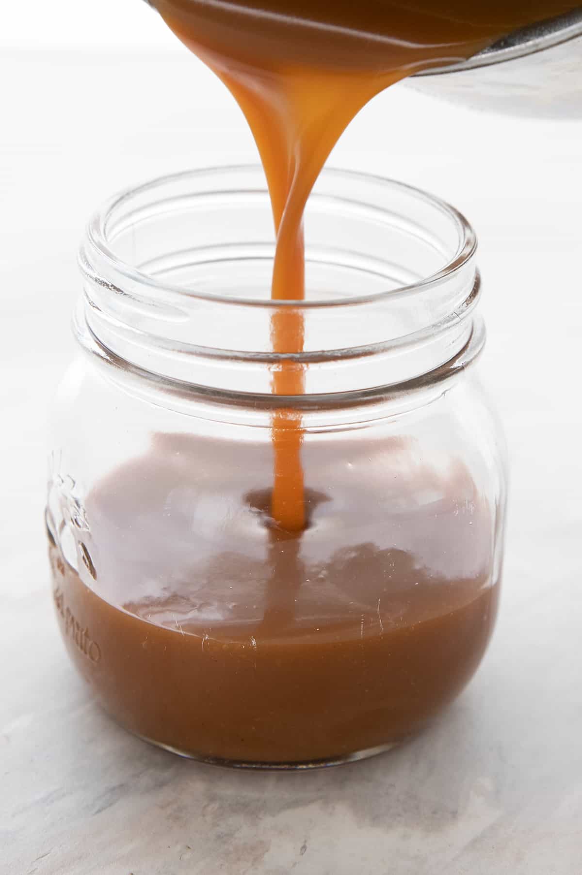 Keto dulce de leche being poured from a pan into a glass jar.