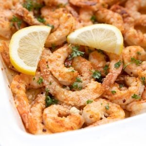 Baked shrimp in a white baking dish with parmesan and lemon slices.