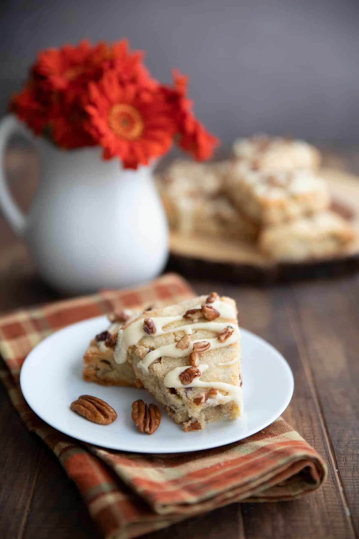 A table scene with keto maple pecan scones in front and orange flowers in a vase.