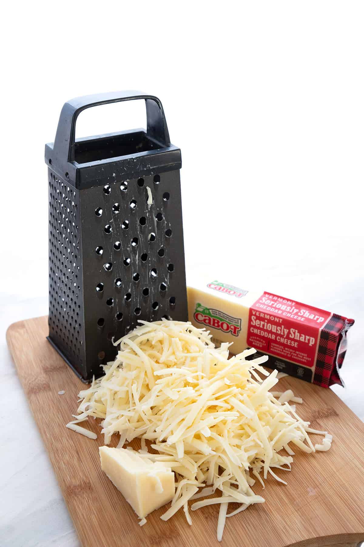 A cutting board with grated cheddar and a cheese grater.