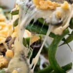 Titled image of a spoon lifting green bean casserole out of a white oval baking dish.