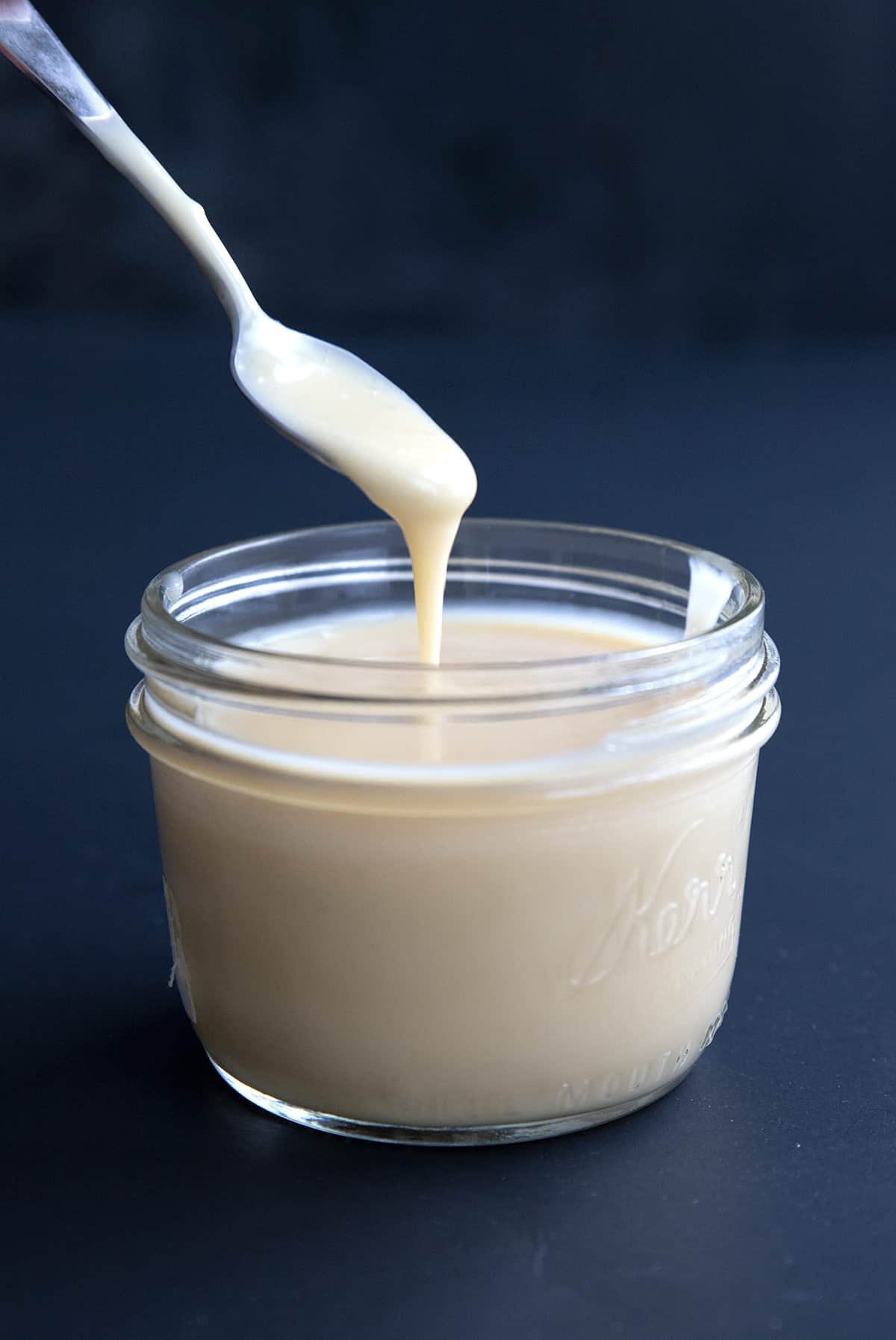 A spoon digging into a jar of Keto Sweetened Condensed Milk.