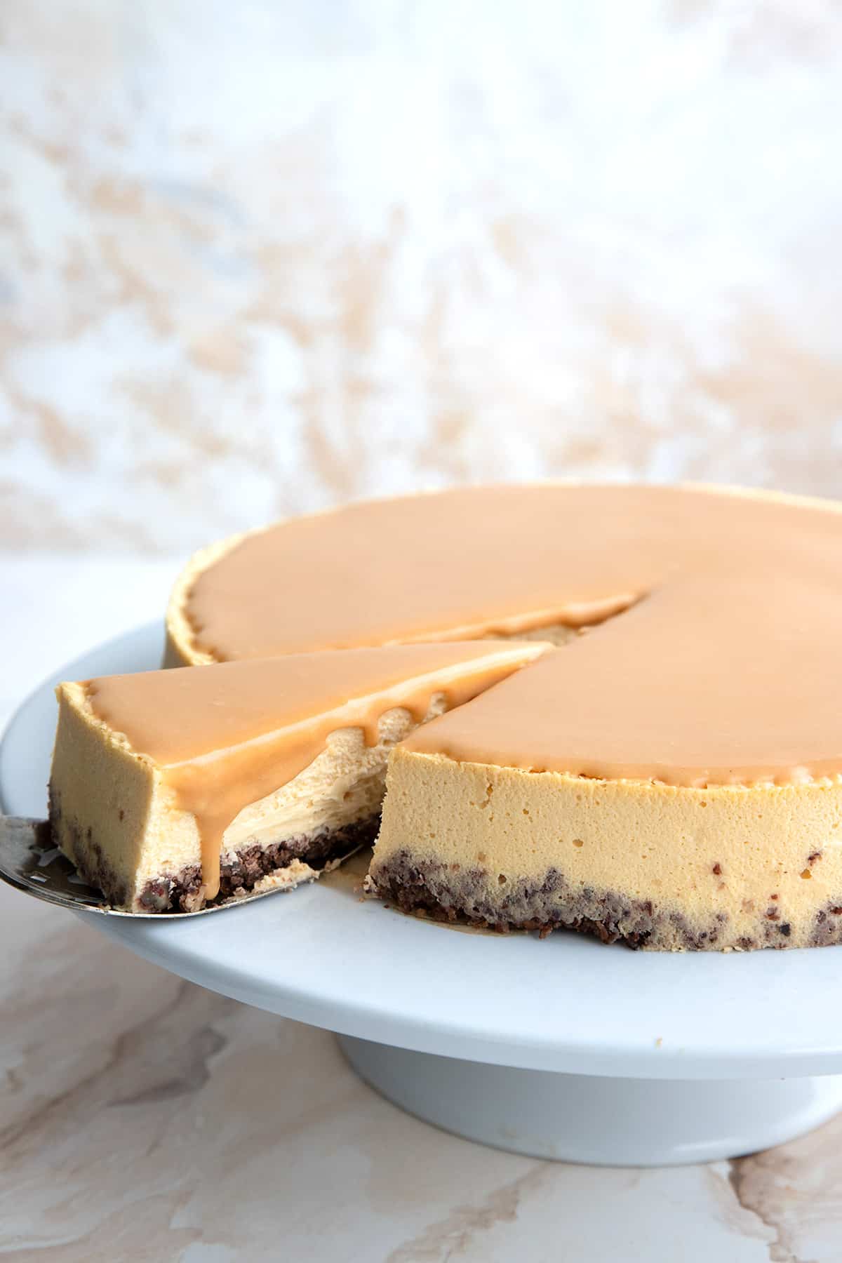 A cake platter with Dulce de Leche Cheesecake, with a slice being lifted out of it.