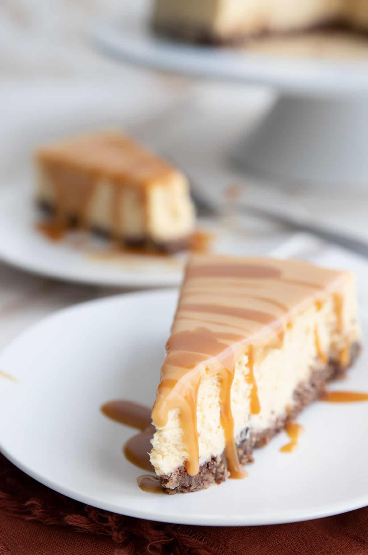 A slice of Dulce de Leche Cheesecake on a white plate with more cake in the background.