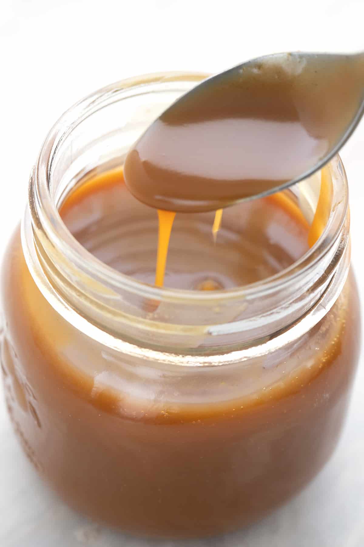 Close up shot of sugar free keto dulce de leche on a spoon above a jar.