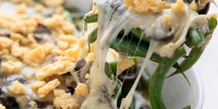 A spoon lifting out some Keto Green Bean Casserole from the dish, with gooey cheese on top.