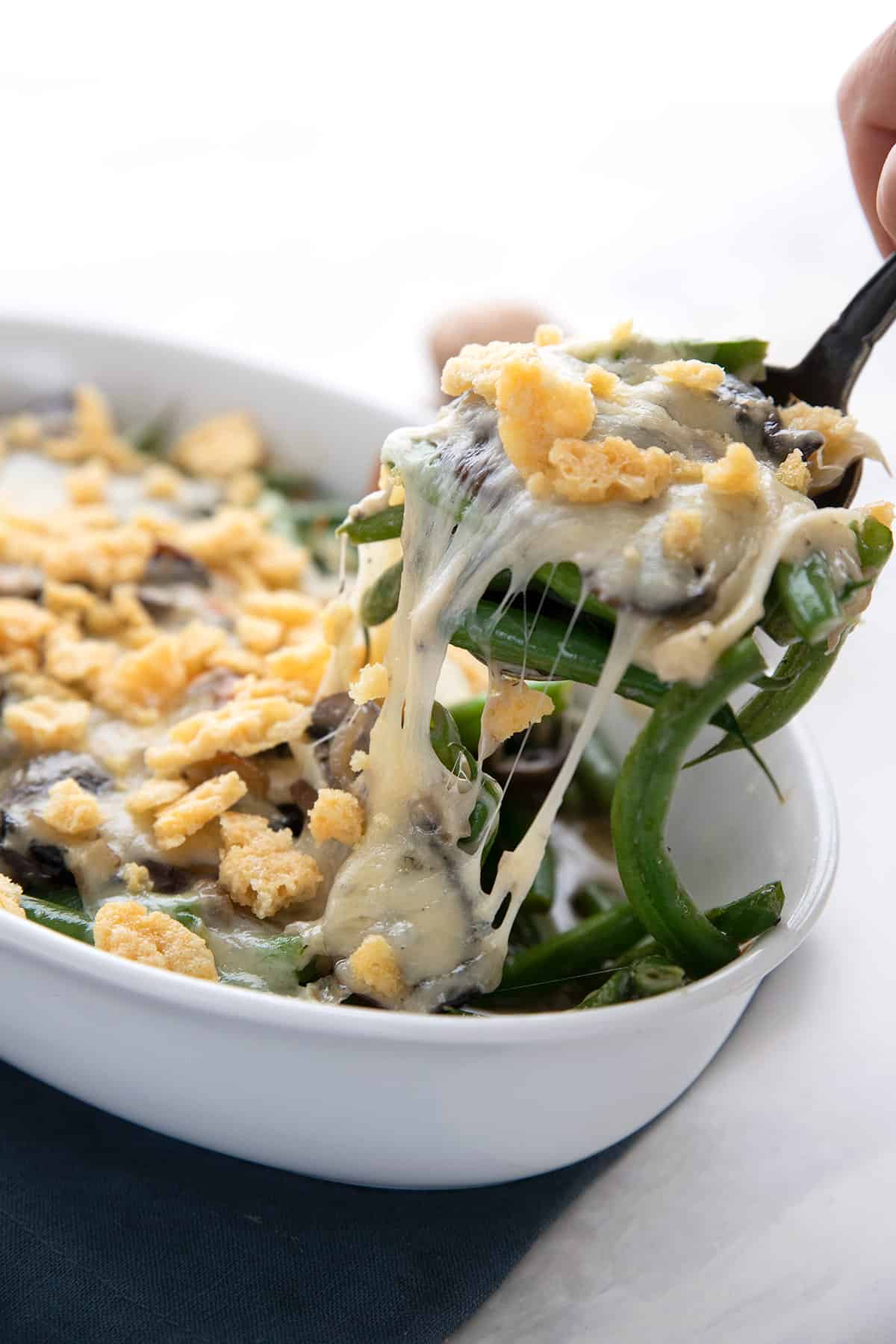 A spoon lifting out some Keto Green Bean Casserole from the dish, with gooey cheese on top.