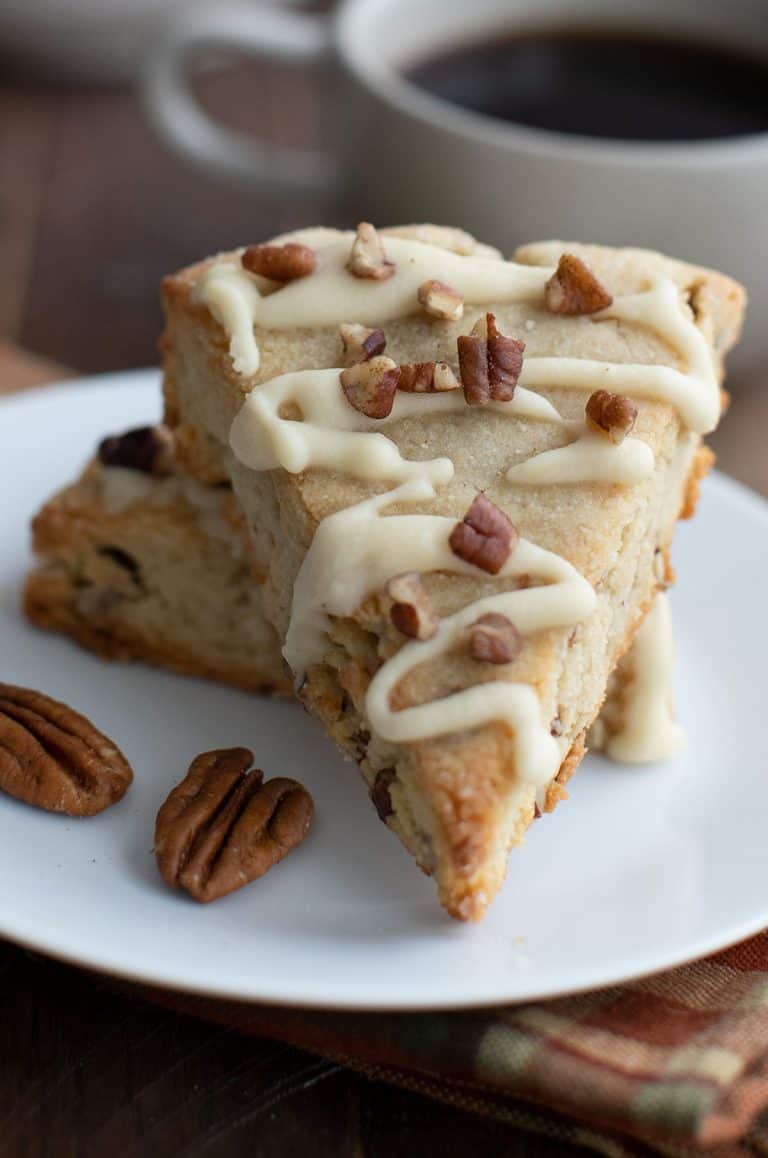 Close up shot of a Keto Maple Pecan Scone on a white plate with a cup of coffee just behind.