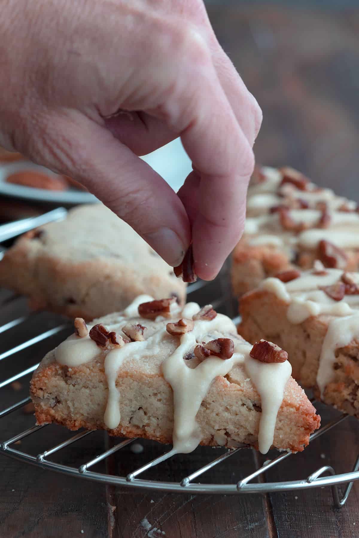 A hand sprinkling chopped pecans over maple pecan scones.