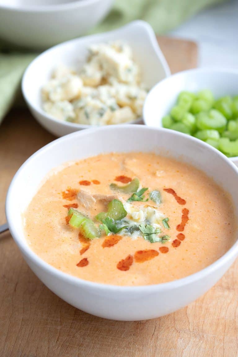 A bowl of Buffalo Chicken Soup on a cutting board with celery and bleu cheese in the background.