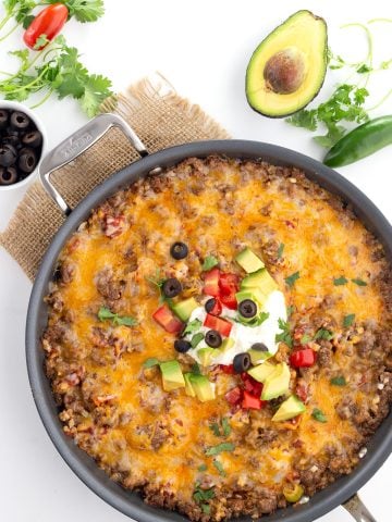 Top down image of Mexican Cauliflower Rice in a large skillet, with avocado, cilantro, jalapeno and olives all around.