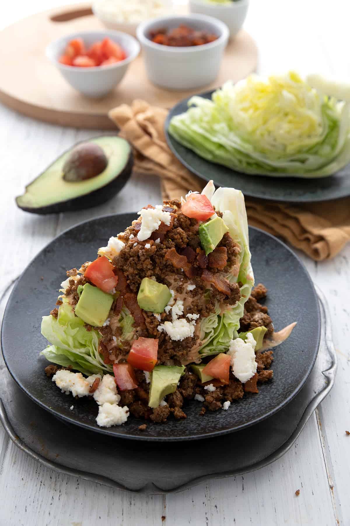 A serving of Mexican Wedge Salad on a black page with toppings in the background.