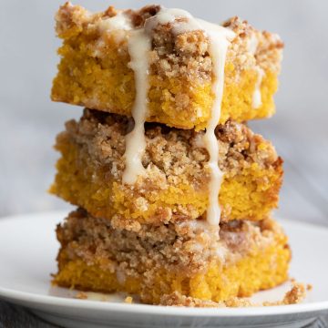 Keto pumpkin crumb cake stacked on a white plate, with glaze drizzling down.