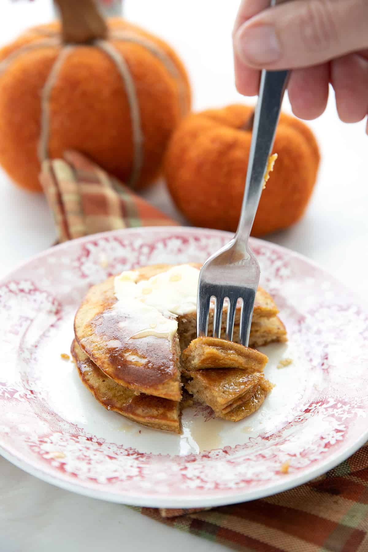 A fork reaching into a plate with two keto pumpkin pancakes.