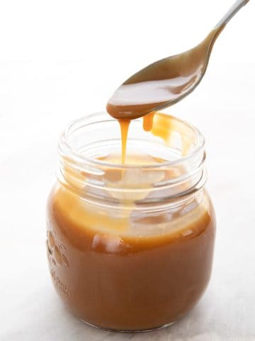 A spoon drizzling keto dulce de leche into a glass jar.